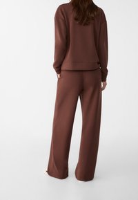 Brun oversized sweatshirt och matchande vida byxor, tillverkade av mjukt material. Har en avslappnad passform och ribbade manschettdetaljer.