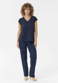 Blouse marine à col en V avec des manches courtes accentuées de dentelle, associée à un jean droit bleu foncé. Tissu lisse avec une coupe décontractée.