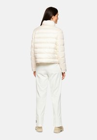 Weiße kurze Steppjacke mit hohem Kragen, mit gesteppter Textur und eingesetzten Ärmeln. Kombiniert mit hellfarbenen, weit geschnittenen Hosen.