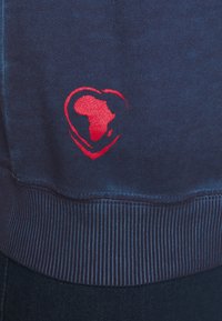 Felpa blu navy con outline di un cuore rosso e una silhouette dell'Africa all'interno. Maniche e orlo a coste, realizzata in un tessuto morbido e texturizzato.