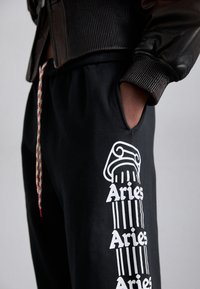 Schwarze Sweatpants mit einem künstlerischen weißen Säulengrafik und Text. Sie verfügen über einen elastischen Bund mit Kordelzug und seitliche Taschen.