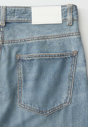 Achterzak van lichtblauwe spijkerbroek met oranje stiksel en een wit rechthoekig label op de tailleband.