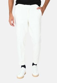 Pantaloni in corduroy bianchi con un design aderente, gambe strette, tasche frontali e chiusura con bottone, abbinati a sneakers bianche.