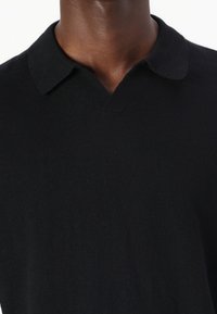 Svart strikket polo-shirt med v-hals og klassisk krage. Stoffet har en jevn tekstur uten synlige mønstre eller detaljer.