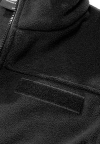 Veste polaire noire avec une fermeture éclair et un patch Velcro rectangulaire sur la poitrine pour fixer des étiquettes nominatives ou d'identification.