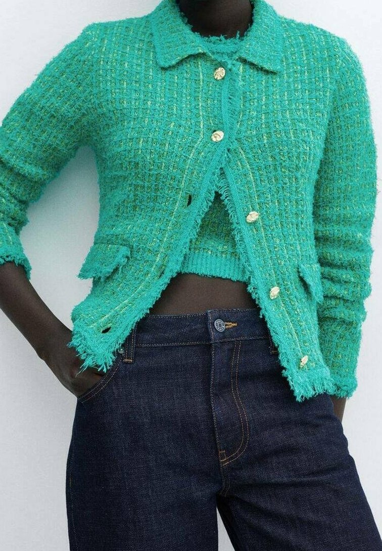 Turkusowy dzianinowy kardigan o fakturze, z złotymi guzikami, naszywanymi kieszeniami i postrzępionymi krawędziami, zestawiony z ciemnoniebieskimi dżinsami.