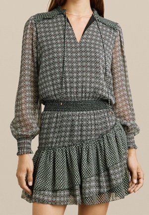 Femme portant un chemisier à manches longues à motifs avec des manches transparentes et une jupe taille haute assortie avec des détails à volants.