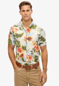 Camisa de manga corta con estampado floral que presenta un fondo azul claro, flores rojas y amarillas vibrantes, hojas verdes y un cuello con botones.