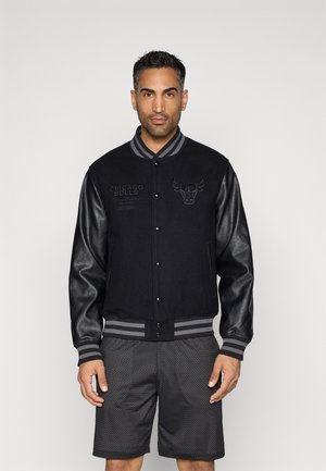 Musta yliopistotakki, jossa on villakebody ja nahka-hihat, varustettuna Chicago Bulls -logolla sekä raidallisilla ribbineulekangas hihansuissa ja helmassa.