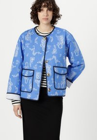 Blue quilted jacket with white floral pattern, rounded neckline, front buttons, and two front pockets. Black trim and striped sleeves visible.