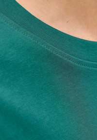 Petrolkleurig katoenen T-shirt met een geribbelde ronde hals, een gladde textuur en lichte stikseldetails langs de boord. Close-up weergave.