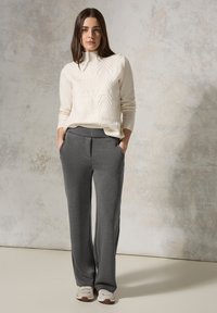 Pull en tricot crème avec un motif en chevrons texturé, associé à un pantalon large gris avec poches latérales et finition lisse.