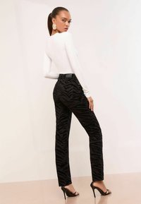 Musta tiigri-printsiga püksid, mis on valmistatud tekstuurilisest kangast, koos sobiva valge pika varrukaga topiga. Kõrgendatud kontsad täiendavad komplekti.