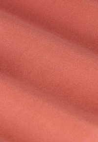 Coral-colored fabric with a smooth, slightly shiny texture, showing gentle waves and light reflections across the surface.