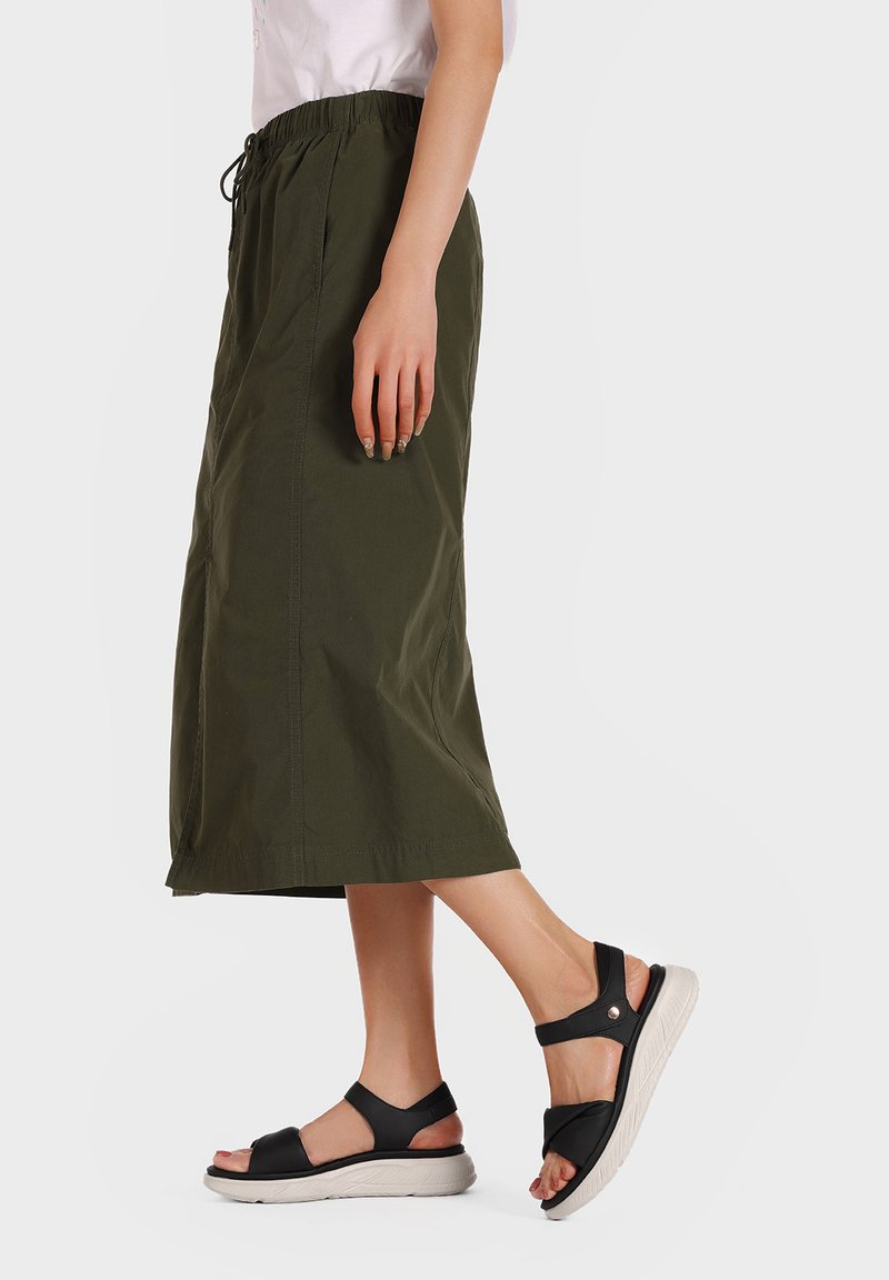 Gonna verde oliva realizzata in tessuto leggero, con vita elastica e coulisse. Abbinata a sandali neri con suola spessa.