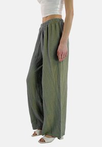 Vida med vida byxor i grön och grå krinklad tyg, med en elastisk midja och en strukturerad yta. Kombineras med vita öppen tå klackar.