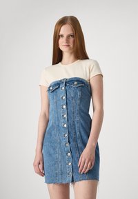 Denim mini kleit, millel on kitsas, nööbiga disain, lisaks helebeežist T-särgi kiht. Kleidil on narmendav äär ja minimaalne kaunistus.