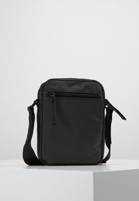 Black crossbody bag made of textured fabric, featuring a front zipper pocket, adjustable strap, and a rectangular design.
