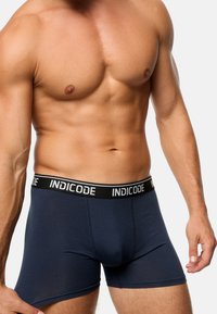 Marineblaue Boxershorts mit einem schwarzen Bündchen, auf dem der Markenname "INDICODE" abgedruckt ist. Weicher, glatter Stoff mit einer figurschmeichelnden Passform.