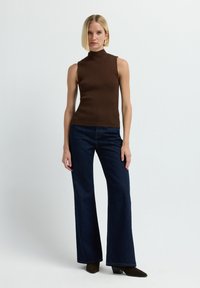 Bruine geribbelde mouwloze top met een hoge kraag, gecombineerd met donkerblauwe uitlopende jeans, gedragen met spitse bruine enkellaarsjes.