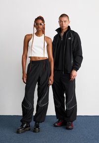 Svart idrettsjakke med hvite detaljer, hvit crop top, svarte bukser med hvite sømmer. Modellene har på seg kraftige svarte og røde sko.