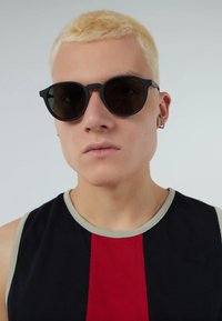 Zwarte ronde zonnebril met donkere lenzen, gecombineerd met een mouwloos zwart tanktop met een rood en grijs ontwerp. Soepele texturen en minimale hardware.