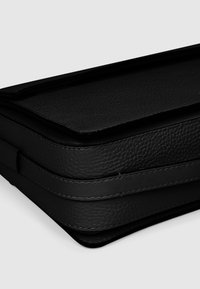 Svart läderväska med en texturerad yta och platt design, med sömmar runt kanterna och en slät klaffstängning, kompakt och rektangulär form.