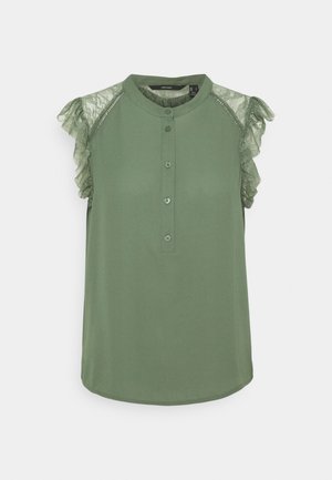 Blouse verte sans manches avec des détails en dentelle volantée sur les épaules, un col rond, et une patte de boutonnage frontale avec quatre boutons.