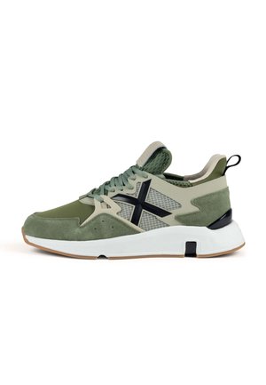 Zapatilla deportiva verde con una parte superior de ante y malla, detalles en negro contrastante, suela exterior de goma texturizada y entresuela acolchada.
