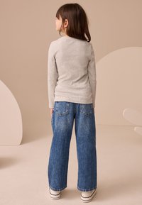 Gray long-sleeve top and loose-fitting blue denim jeans with back pockets, paired with white sneakers featuring black stripes.