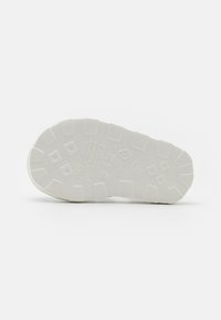 Fehér gumi cipőtalp texturált mintázattal, körkörös és téglalap alakú gumírozott részekkel a tapadás érdekében, valamint gravírozott márka- és méretinformációkkal.