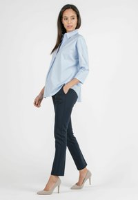Himmelblaues Hemd mit aufgerollten 3/4-Ärmeln, kombiniert mit navyblauen Slim-Fit-Hosen und beigen High Heels. Glatter Stoff, lässiges Design.