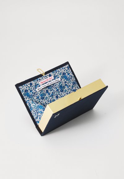 Clutch din material bleu marin cu un clasp de nuanță aurie, având un interior cu un model floral în nuanțe de albastru și alb. Eticheta indică faptul că este realizat manual în Italia.
