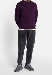 Lilla strikket sweater, grå teksturerede jeans og grå sneakers. Outfittet indeholder en hvid t-shirt under sweateren.