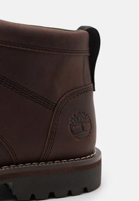 Bottines en cuir marron avec une finition texturée, dotées d'une languette noire contrastante, d'une couture contrastante et d'un logo arbre en marque sur le côté.