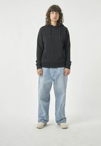 Schwarzer Kapuzenpullover mit einer Vordertasche, kombiniert mit hellblauen, weiten Jeans. Der Stoff wirkt weich, hat eine entspannte Passform und gerippte Bündchen.