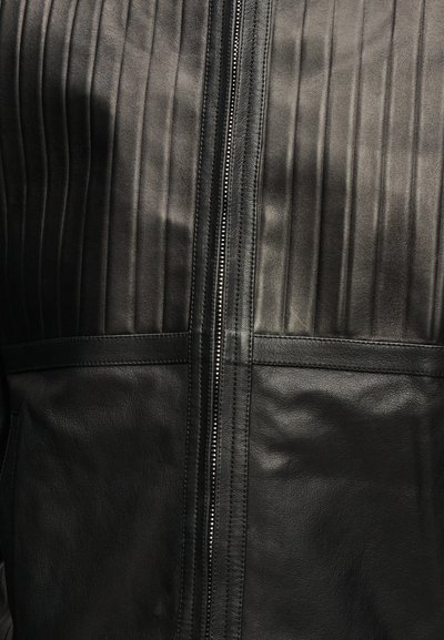 Μαύρο δερμάτινο μπουφάν με κάθετα ραμμένα πάνελ στο επάνω μέρος και λείο δέρμα στο κάτω μέρος, με κεντρικό ασημένιο φερμουάρ.