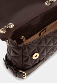 Sac à main matelassé marron avec quincaillerie dorée, comprenant une fermeture à pression et une poche intérieure zippée. Cuir synthétique lisse avec une forme structurée.