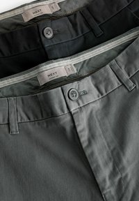 Deux paires de pantalons skinny, l'une en gris foncé et l'autre en noir. Les caractéristiques incluent des boutons, des coutures détaillées et des étiquettes en tissu.