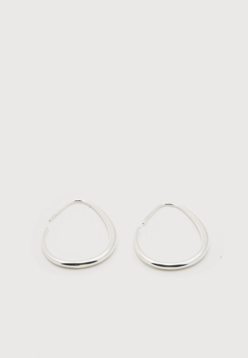 Ζευγάρι λείων, καμπυλωτών ασημένιων σκουλαρικιών σε σχήμα κρίκου με ανοιχτά άκρα, που ακουμπούν επίπεδα σε απλό λευκό φόντο.