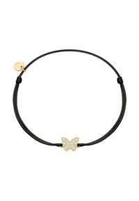 Melnā ādas aproce ar zelta tauriņu piekariņu, kas rotāts ar caurspīdīgām kristālām. Vienkārša mezgla aizdare vienā pusē, pievienots logotipa uzraksts.