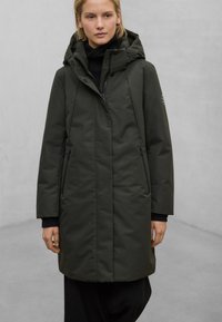 Tmavě zelený dlouhý zateplený kabát s kapucí, předním zipem a bočními kapsami. Má elegantní design a jemnou texturu.