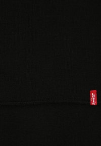 Tejido de punto negro con una textura suave, que presenta una etiqueta del logo rojo de Levi's en la esquina inferior derecha y un sutil detalle de costura.