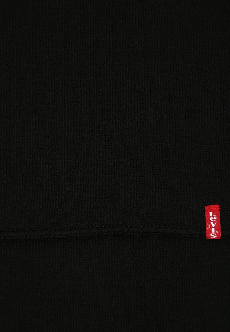Tissu tricot noir avec une texture lisse, comportant une étiquette logo rouge Levi's dans le coin inférieur droit et un détail de couture discret.