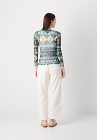 Maglietta a maniche lunghe, aderente, con un motivo geometrico multicolore che presenta lanterne, abbinata a pantaloni bianchi larghi e scarpe multicolori.