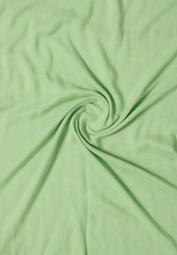 Tissu vert clair torsadé en forme de spirale, montrant une texture douce et des plis légers irradiant depuis le centre.