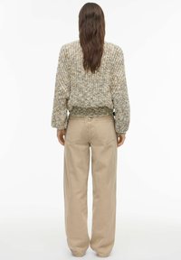 Pull en maille aux tons neutres avec design texturé et ourlet côtelé, associé à un pantalon ample beige clair avec poches arrière.