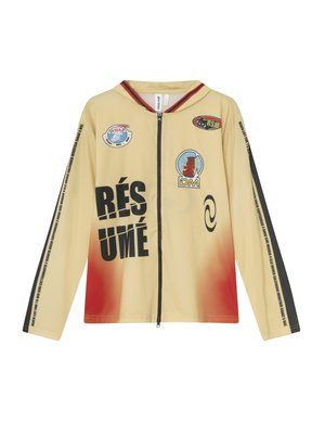 Beige jas met lange mouwen en ritssluiting, voorzien van een rode gradient, zwarte grafische tekst en meerdere logo's op de voorkant en mouwen, gemaakt van lichtgewicht stof.