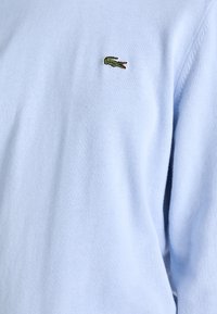 Jasnoniebieski sweter wykonany z miękkiego materiału o prążkowanej fakturze. Na piersi ma małe zielone logo krokodyla.