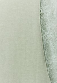 Tessuto verde chiaro con un motivo lavorato a maglia su un lato e un delicato bordo in pizzo sull'altro, che mostra un contrasto tra superfici lisce e testurizzate.